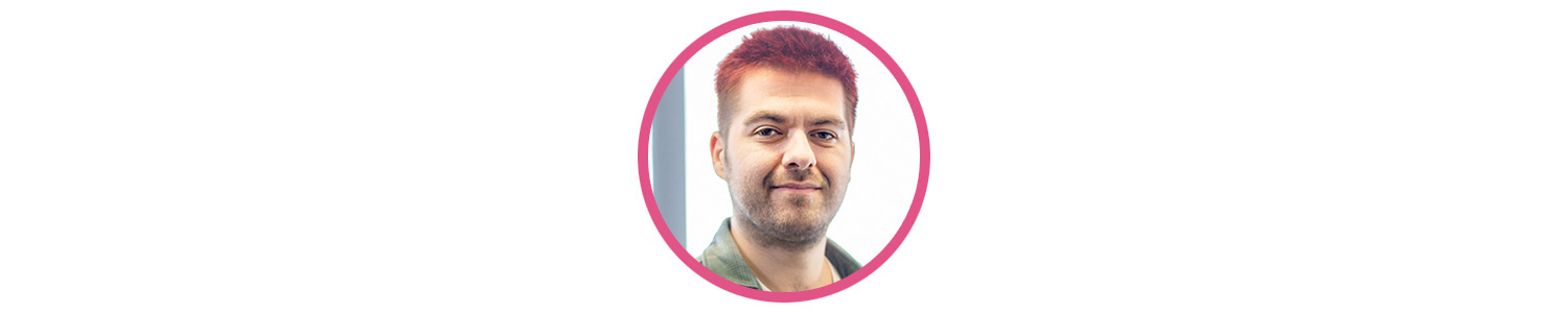 Photo of Joseph 'JLR' Lewis Reid, a white male with stubble and dyed pink short hair. He is smirking at the camera.