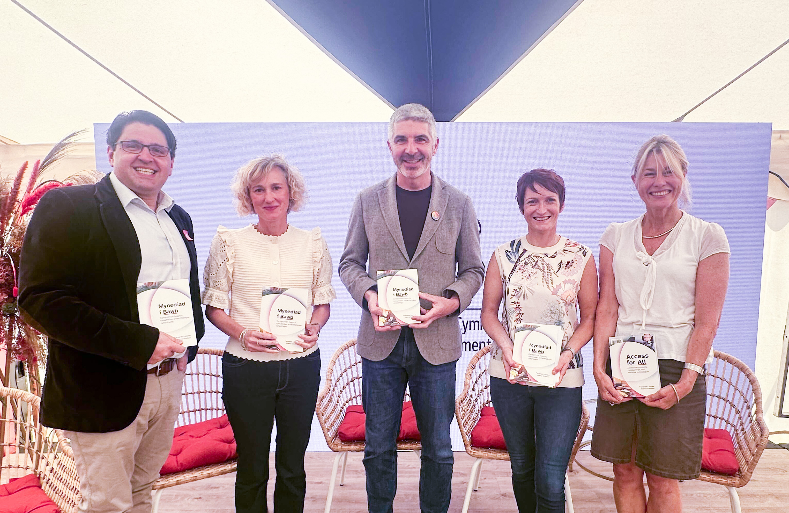 John Mark-Frost, CDPS Interim Chair, Efa Gruffudd, the Welsh Language Commissioner, Derek Walker, The Future Generations Commissioner, Rhian Bowen Davies, The Older People's Commissioner for Wales and Myra Hunt, joint CEO at CDPS stand in a line on the stage at the Eisteddfod in the Welsh Government tent. They're each holding a copy of the 'Access for All' book.